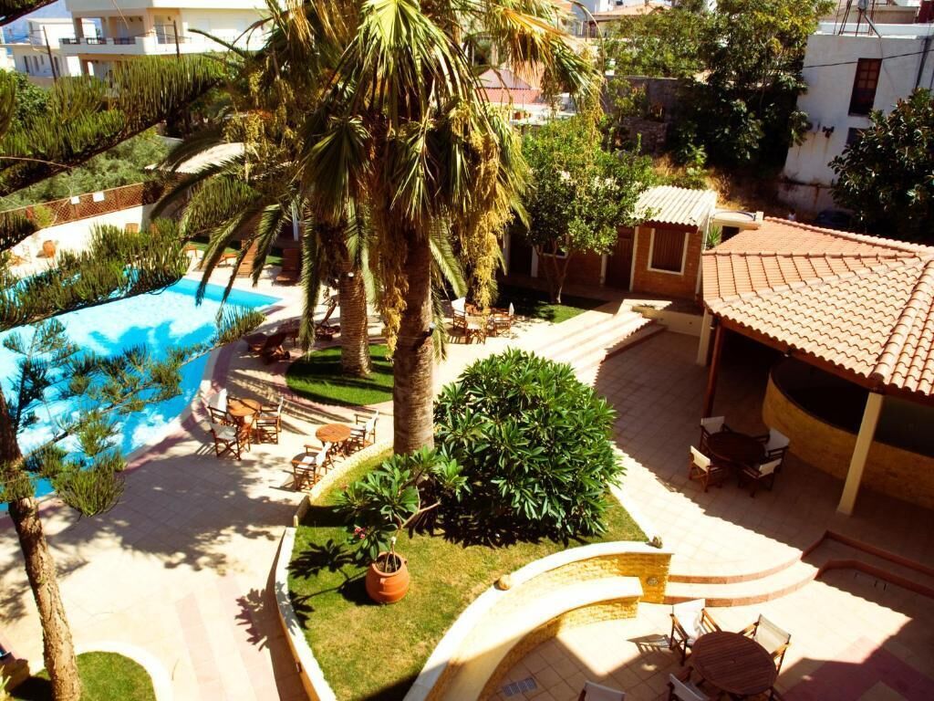 A pool area with lounge chairs and a palm tree, surrounded by greenery and a tiled roof structure.