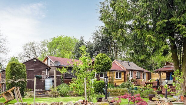 A row of wooden houses with brick walls, a brick wall with rocks, and a grassy lawn. - Woodcarver's Cottage (Spring Village)