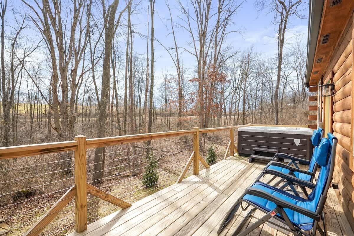A wooden deck with a hot tub, two blue lounge chairs, and a view of a forest.