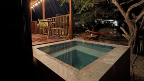 Une piscine avec une terrasse en bois et des chaises, entourée d’arbres.