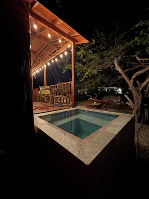 Una piscina con un solarium in legno e sedie, immersa nel verde.
