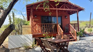 Une cabane en bois dotée d’un balcon, d’un espace extérieur aménagé et offrant une vue sur des cactus et un paysage désertique.
