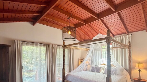 Un lit à baldaquin, un parquet en bois, un canapé avec des coussins et une fenêtre avec des rideaux.