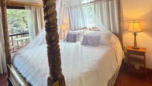Un lit à baldaquin, une table de chevet avec une lampe et une vue sur l’extérieur par une fenêtre.