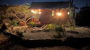 Une cabane en bois dotée d’une véranda, entourée de la végétation désertique et de cactus.