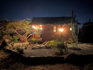 Una casetta di legno con un portico, immersa nella vegetazione desertica e circondata da cactus.