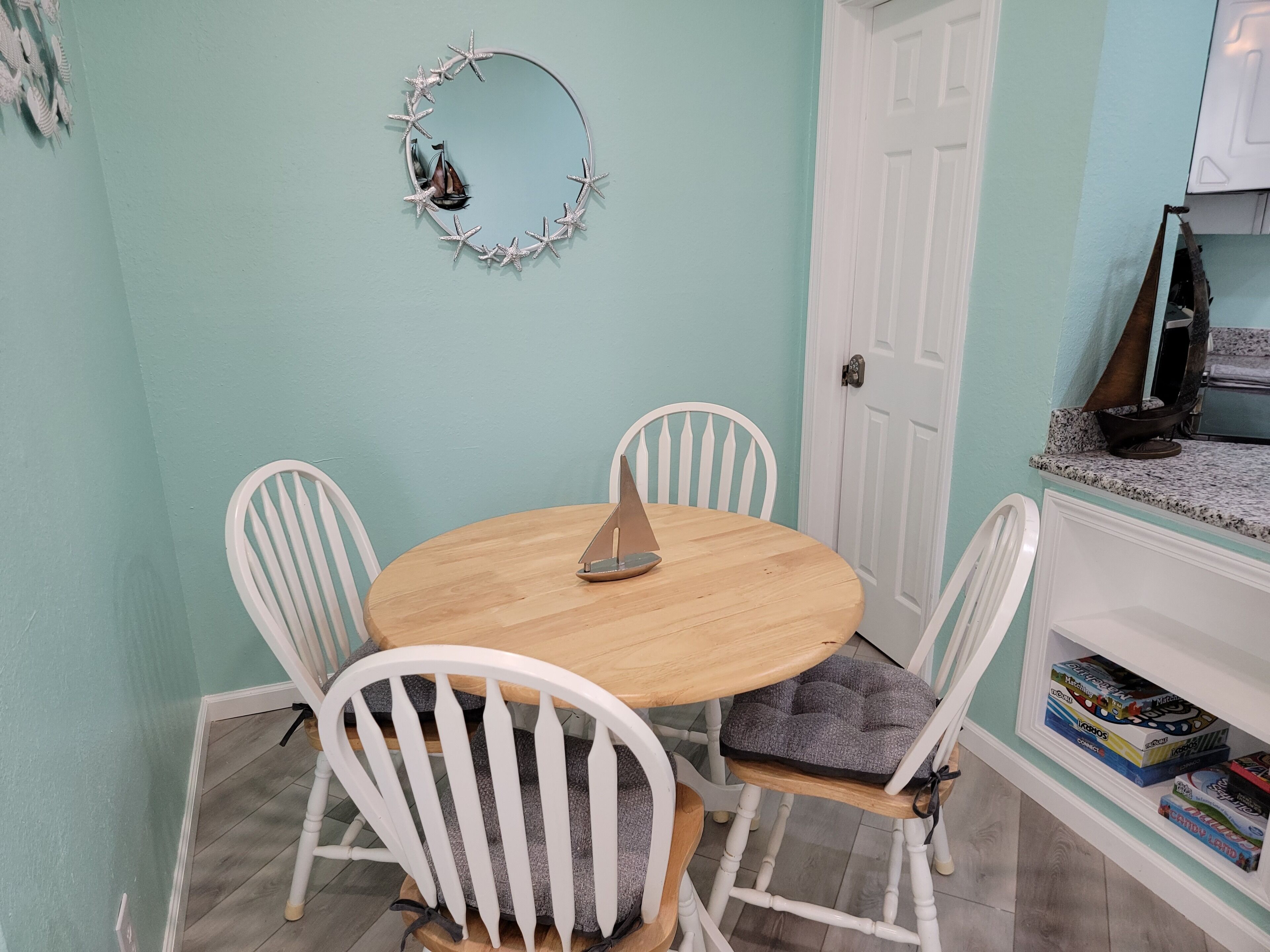 A dining area with a round wooden table, white chairs, and a decorative wall piece.