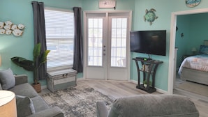 Sala de estar con paredes color aguamarina, ventilador de techo, televisor de pantalla plana, sofá, mesa de centro y una puerta que da a otra habitación.