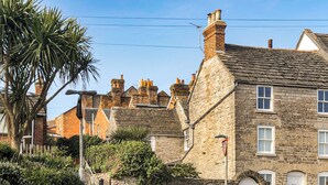 A stone building with a white door, a stone wall, and a palm tree. - 3 bedroom accommodation in Swanage (Swanage)