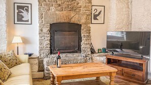 A cozy living room with a stone fireplace, a wooden coffee table, a sofa, and a television. - 3 bedroom accommodation in Swanage (Swanage)