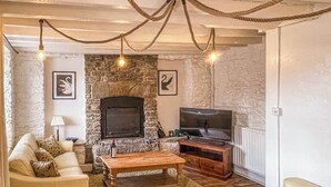 A cozy living room with a stone fireplace, a television, and a wooden coffee table. - 3 bedroom accommodation in Swanage (Swanage)