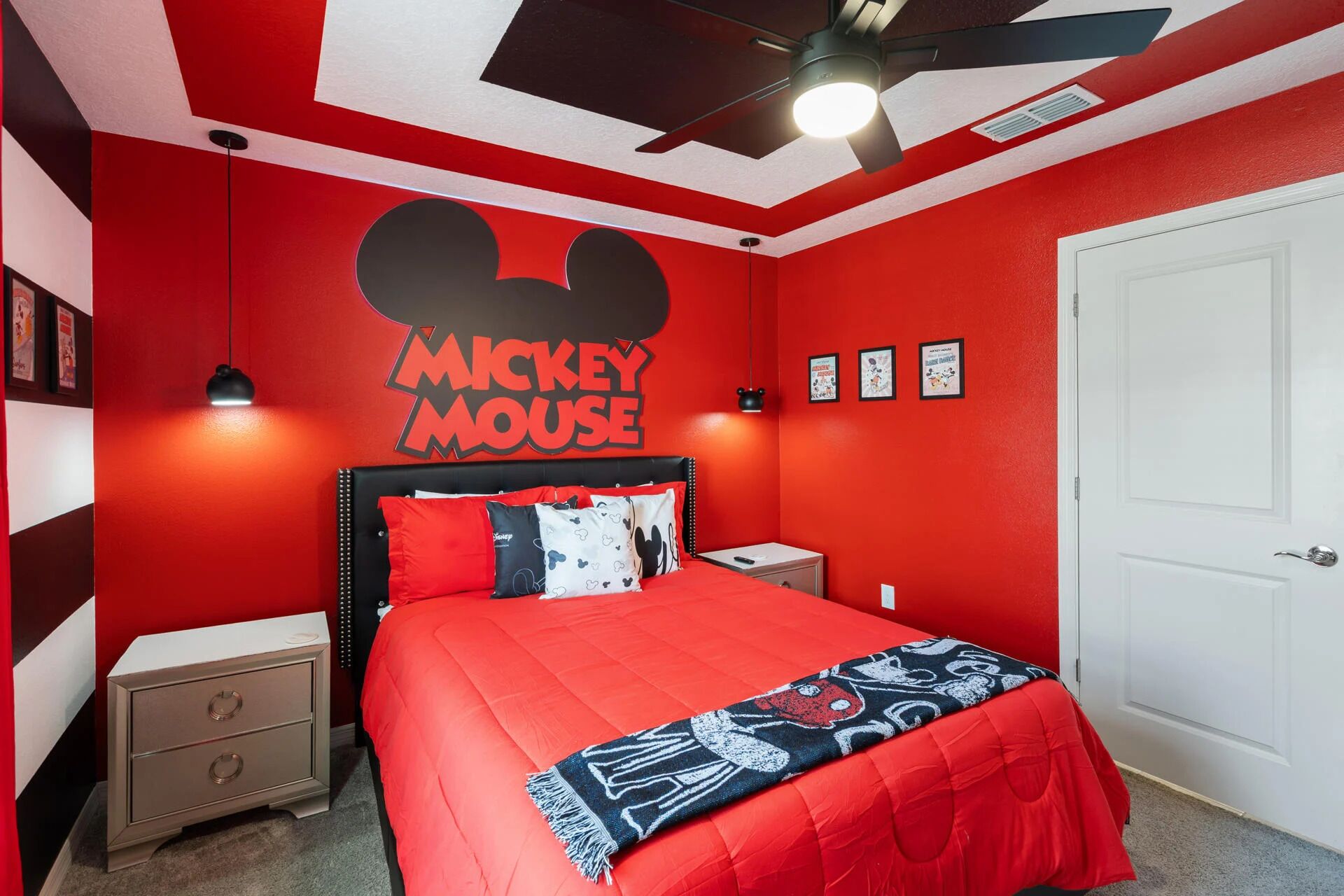 A red-themed bedroom with Mickey Mouse decor, a bed, nightstands, and a white door.