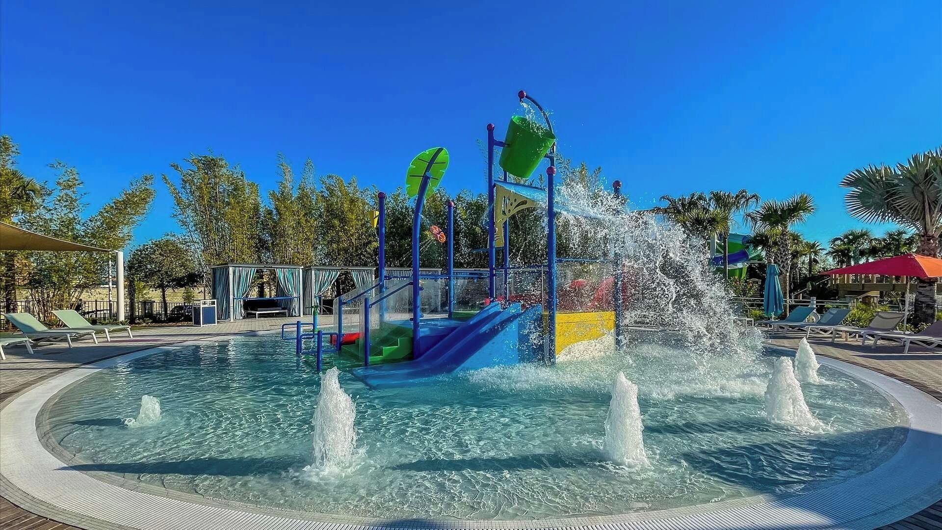 A water park with a central play structure, multiple water jets, and a pool area with lounge chairs.