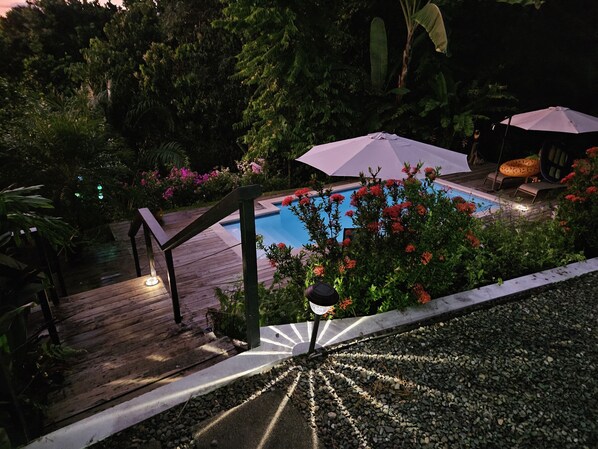 A pool area with a wooden deck, a white pathway, and a stone border.