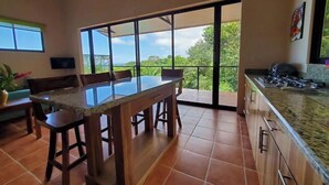 Une cuisine spacieuse avec une grande table à manger, un ventilateur de plafond et une vue sur une végétation luxuriante.