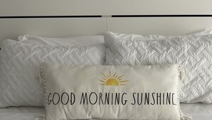 Un lit avec une couette blanche matelassée et un oreiller orné du texte « BONJOUR, RAYON DE SOLEIL » et d’un motif représentant un soleil.