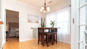 A room with wooden flooring, a dining table with chairs, a chandelier, a bed with a headboard, and a window with curtains. -  Cozy Creekwood Getaway on the Highway (Rehoboth Beach)