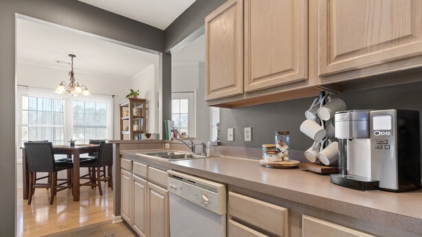 A modern kitchen with wooden cabinets, a dishwasher, a coffee maker, and a dining area with a chandelier. -  Cozy Creekwood Getaway on the Highway (Rehoboth Beach)