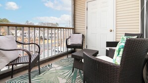 A balcony with wicker furniture, a white door, and a view of a parking lot. -  Cozy Creekwood Getaway on the Highway (Rehoboth Beach)
