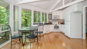 A spacious kitchen with white cabinetry, a dining area with a glass table and chairs, and large windows offering a view of greenery. - Terrific home for a getaway! (Hot Springs)