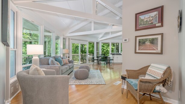 A spacious living room with a large window, a sofa, a chair, and a dining area visible through the glass ceiling. - Terrific home for a getaway! (Hot Springs)