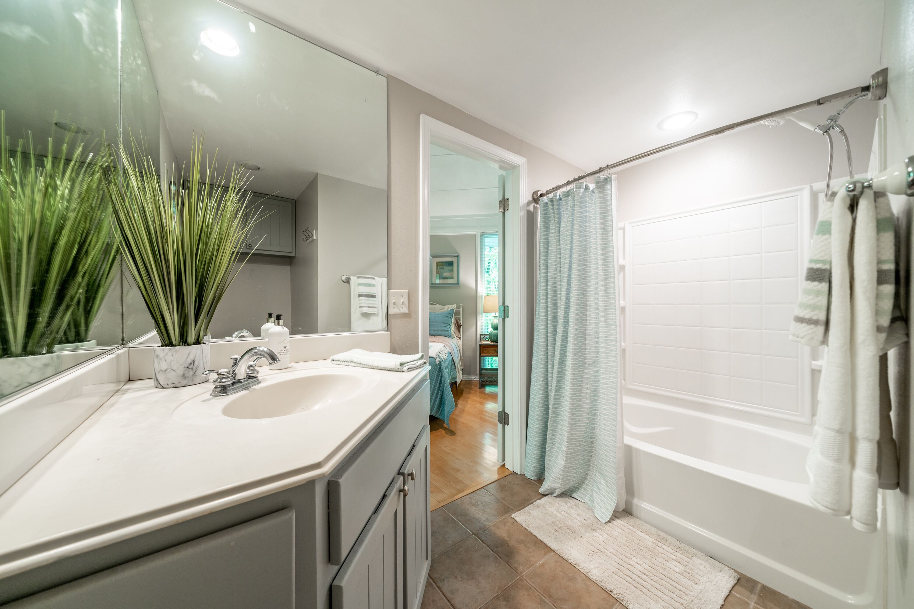 A modern bathroom with a large mirror, white sink, and bathtub.