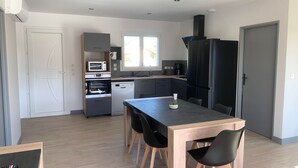 A modern kitchen with built-in appliances, a dining area with a wooden table and black chairs, and a view of the outside through a window. - House sleeps 4 with heated indoor pool ( Maison L'Estuaire) (Grayan-et-l'Hôpital)