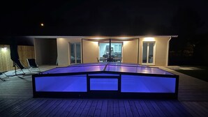A rectangular pool with a dark blue illuminated bottom, surrounded by a wooden deck. - House sleeps 4 with heated indoor pool ( Maison L'Estuaire) (Grayan-et-l'Hôpital)