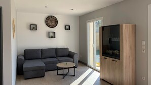 A modern living room with a grey sectional sofa, a round coffee table, a wooden cabinet, and a large wall clock. - House sleeps 4 with heated indoor pool ( Maison L'Estuaire) (Grayan-et-l'Hôpital)