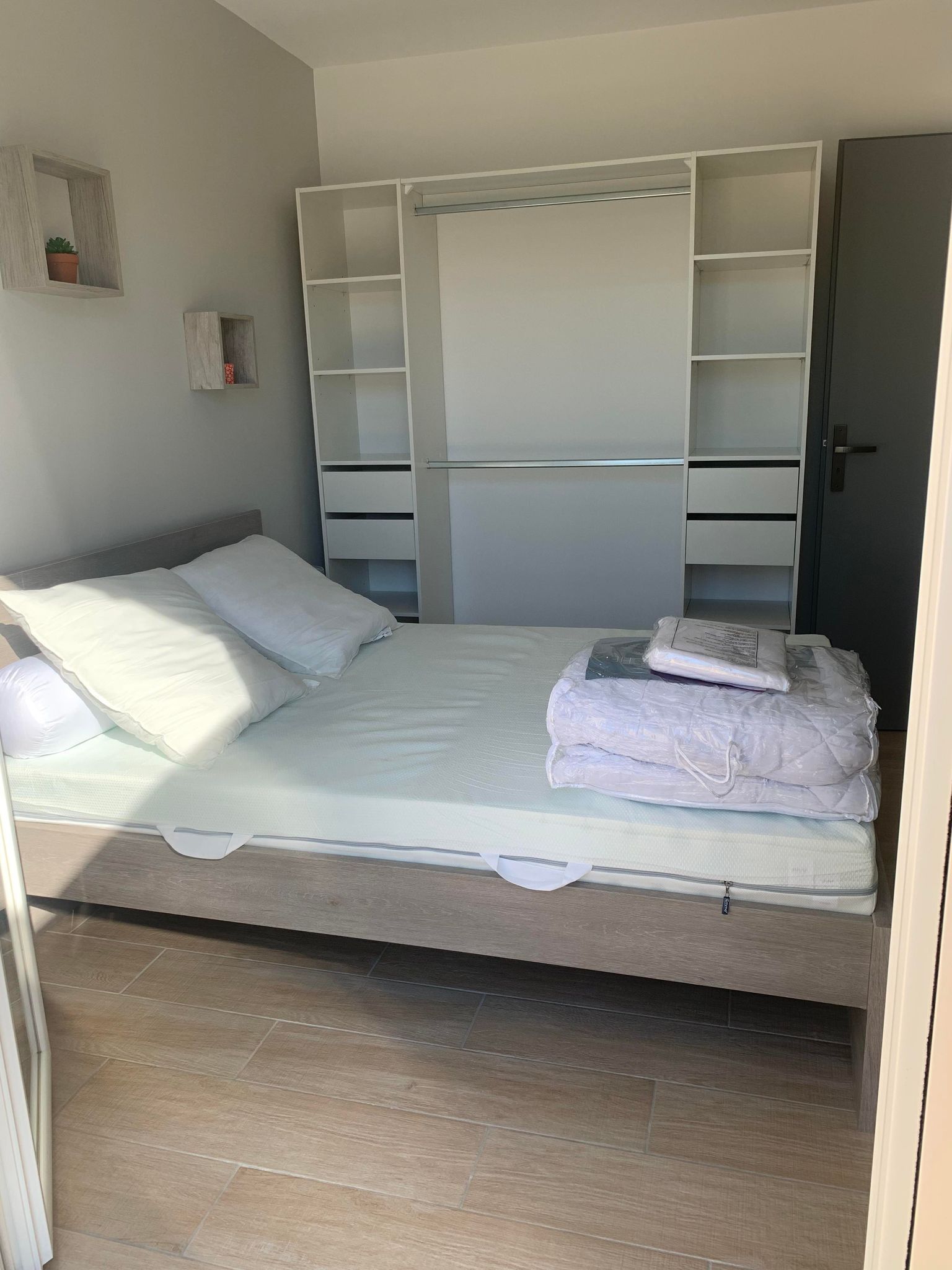 Ein Schlafzimmer mit Bett, Kleiderschrank und einem kleinen Regal mit einer Pflanze.