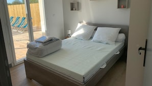 A bedroom with a bed, a nightstand, and a view of an outdoor area with chairs. - House sleeps 4 with heated indoor pool ( Maison L'Estuaire) (Grayan-et-l'Hôpital)