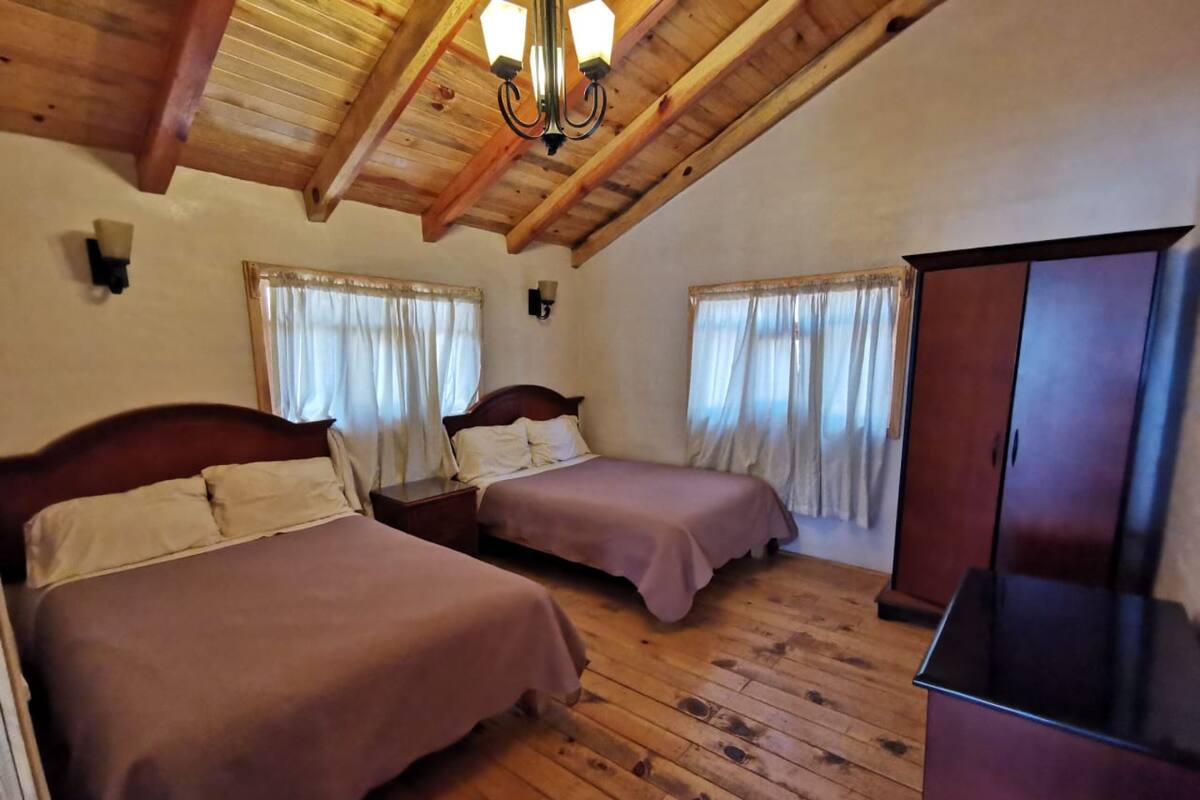 A room with two beds, wooden flooring, a wardrobe, and a chandelier.
