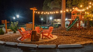 Een terras met houten stoelen en een tafel, omgeven door bomen en lichtslingers.