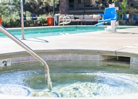 A swimming pool with a metal ladder, a blue chair, and a tiled deck.