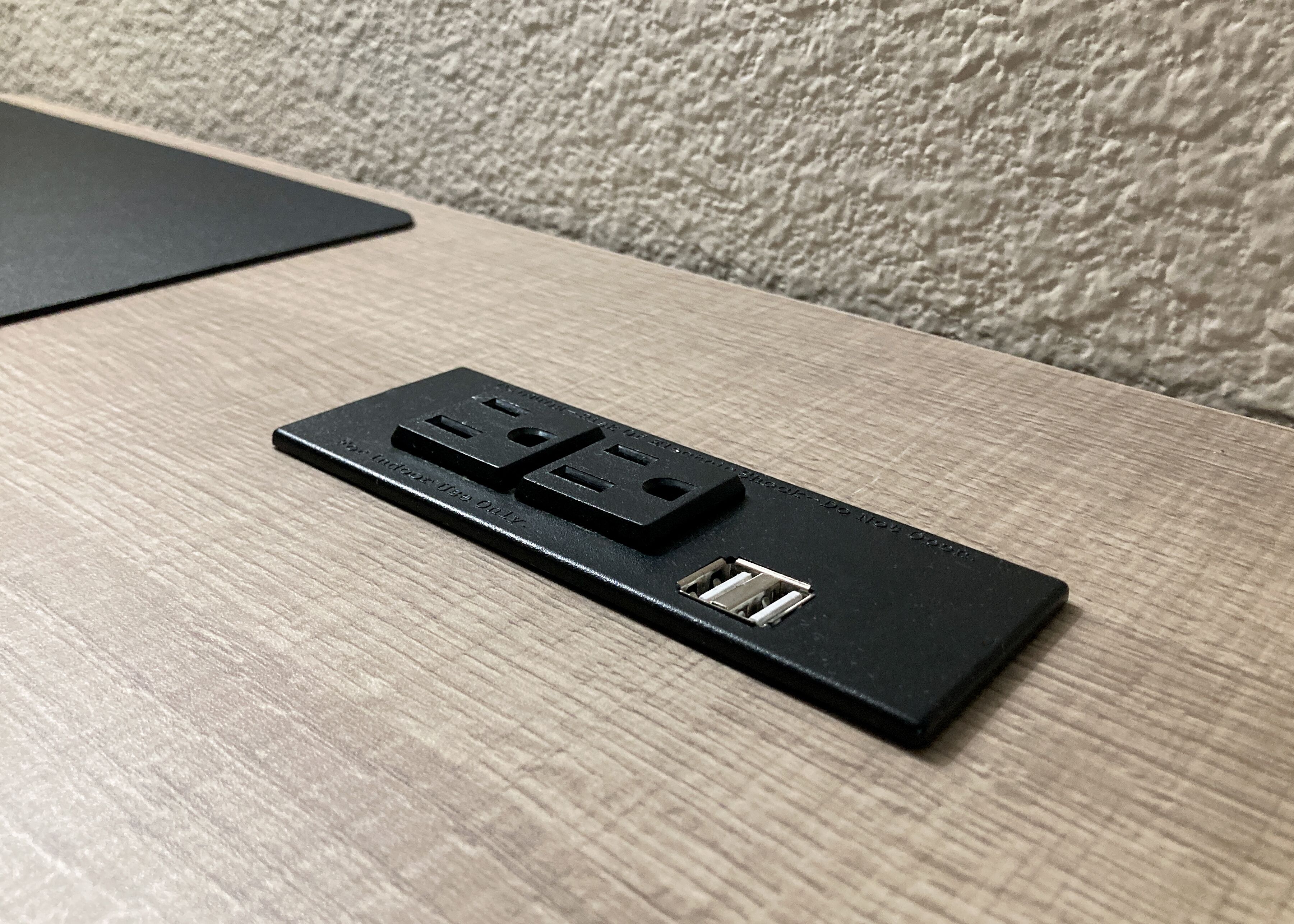 Eine schwarze Mehrfachsteckdose mit zwei USB-Anschlüssen und einer Steckdose auf einer Holzoberfläche.