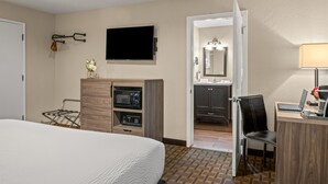 Een hotelkamer met een bed, een bureau met een computer, een televisie, een magnetron en een badkamer die door een open deur zichtbaar is.