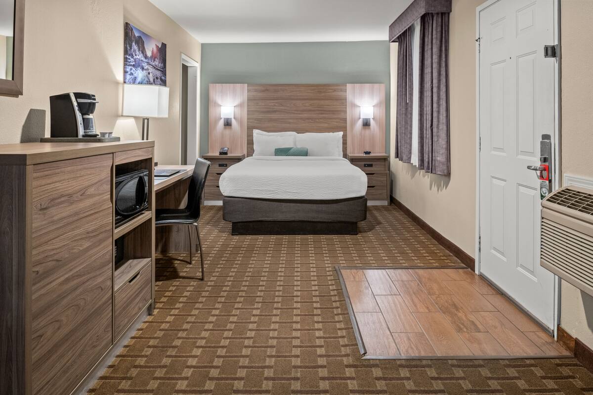 A hotel room with a bed, desk, chair, and a coffee machine.