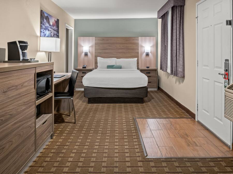 A hotel room with a bed, desk, chair, and a coffee machine.