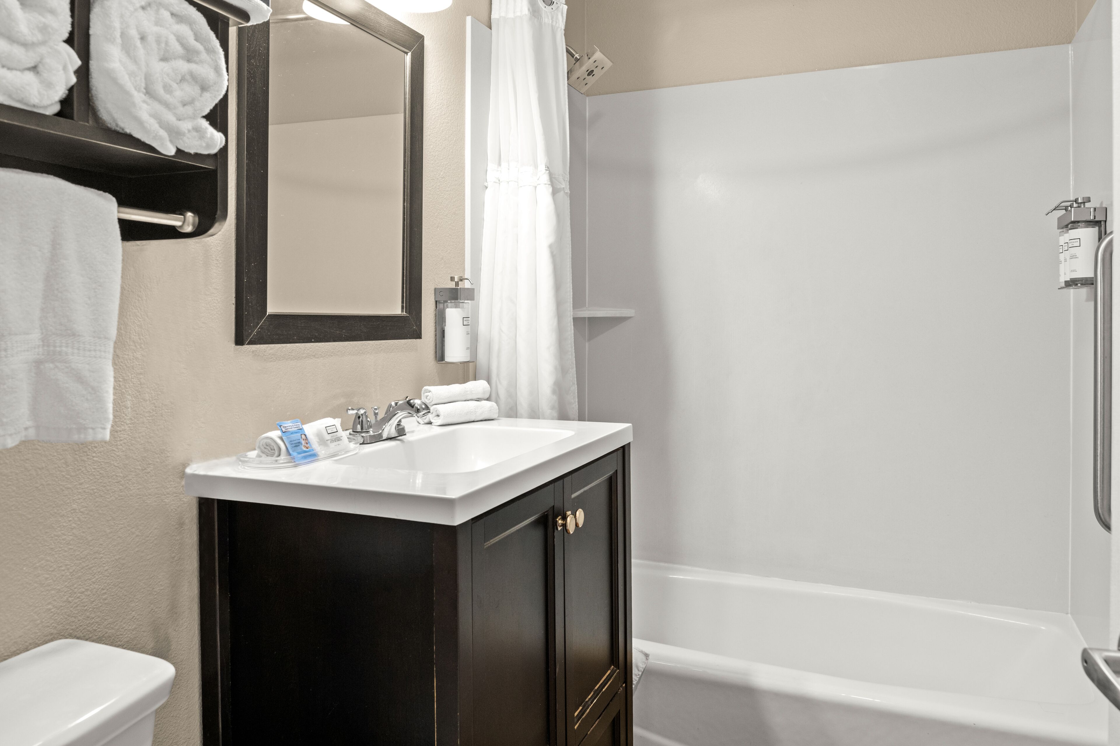 A bathroom with a white sink, dark wooden cabinet, a mirror, a shower curtain, and a toilet.