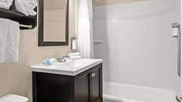 Une salle de bain avec un lavabo blanc, un meuble en bois foncé, un miroir, un rideau de douche et des toilettes.