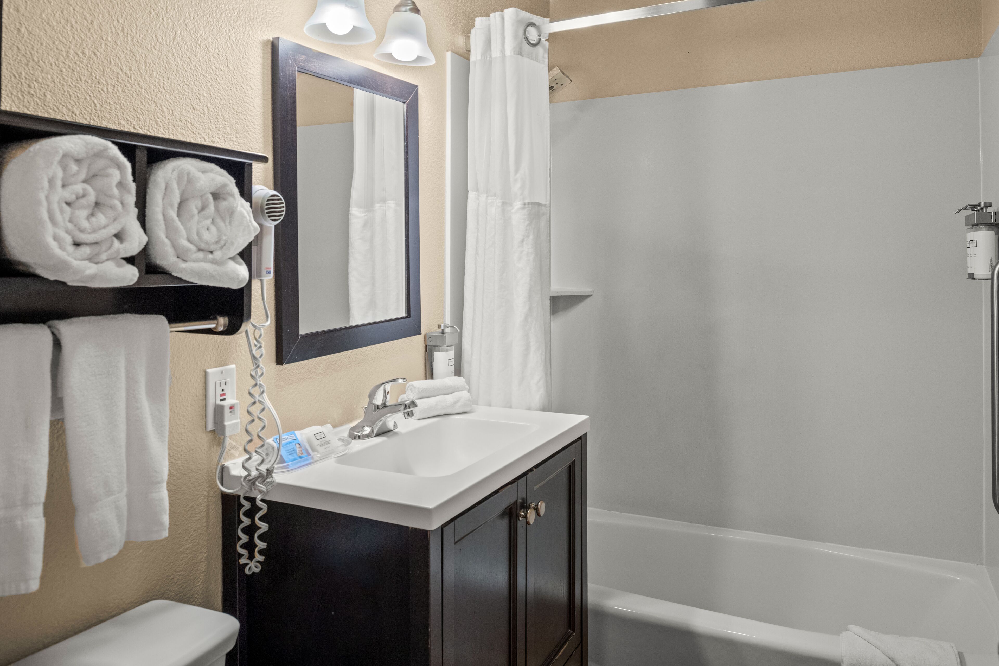 Un baño con un lavabo blanco, un mueble de almacenamiento oscuro y una zona de ducha.