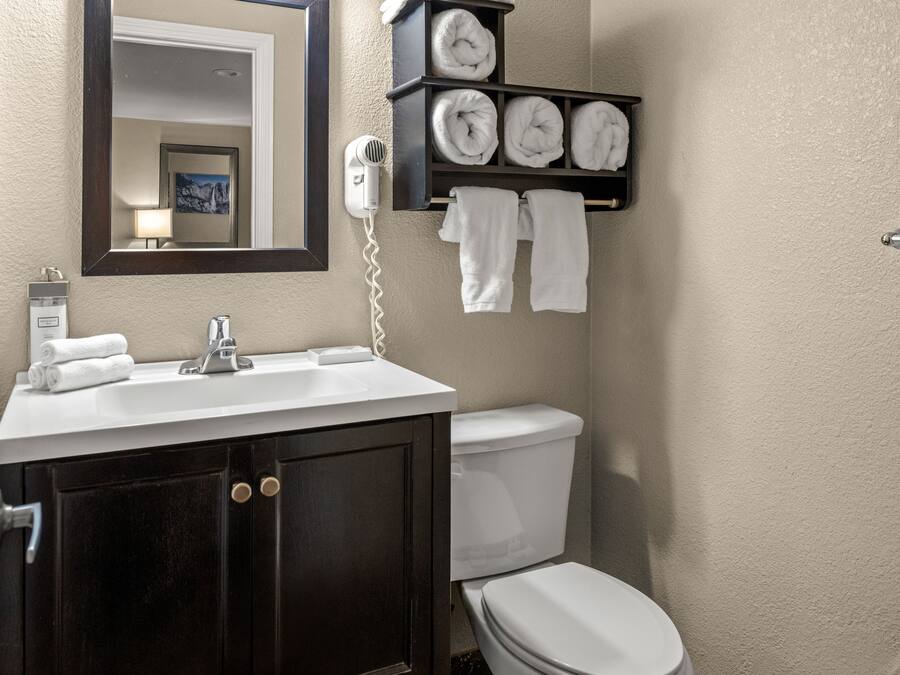 Un bagno con un mobile vanitario in legno scuro, un lavabo bianco, uno specchio, un porta asciugamani con asciugamani piegati con cura e un water.