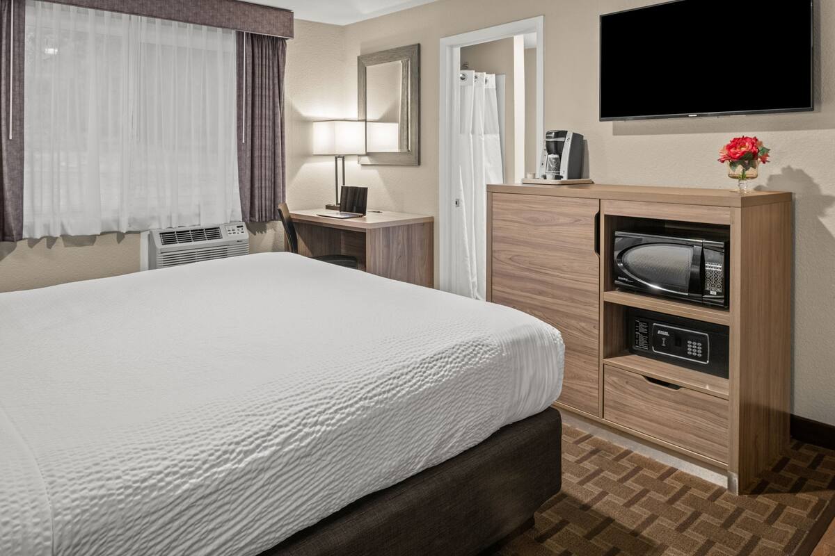 A hotel room with a bed, a desk with a lamp, a microwave, and a TV.
