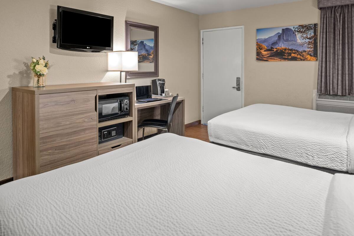 A hotel room with two beds, a desk with a computer, a TV, and a painting on the wall.