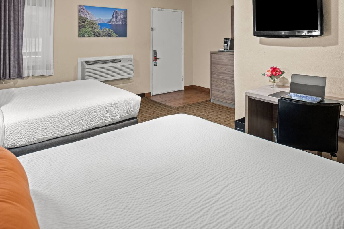 A hotel room with two beds, a desk with a laptop, a TV, and a painting on the wall.