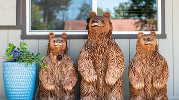 Trois sculptures d’ours en bois sont disposées sur un porche, avec un pot de fleurs bleu à texture sur le côté gauche.