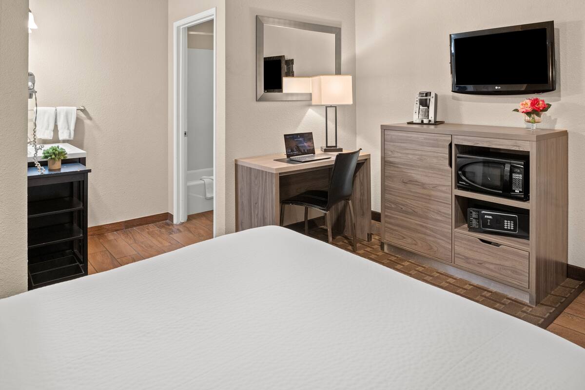 A hotel room with a bed, a desk with a laptop, a TV, a microwave, and a cabinet.