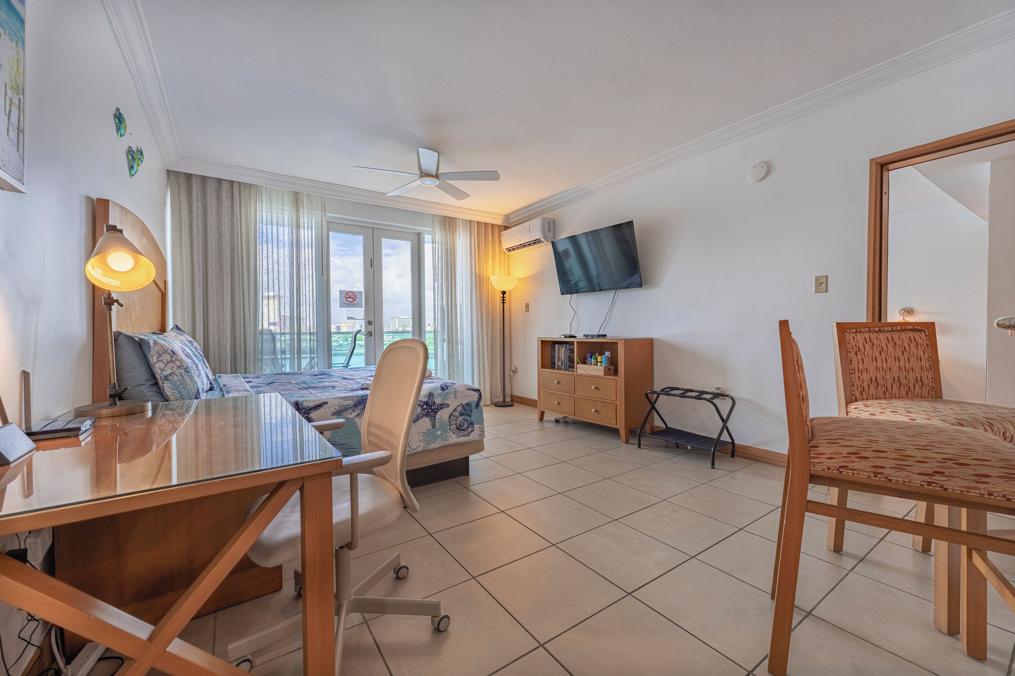 Een hotelkamer met een bed, een bureau, een stoel, een televisie en een balkon met gordijnen.
