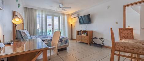 Een hotelkamer met een bed, een bureau, een stoel, een televisie en een balkon met gordijnen.