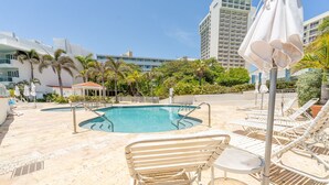 A pool area with lounge chairs and umbrellas, surrounded by palm trees and buildings. - Condado Lagoon Villas/Connected Bayfront Studios w/views, kitchen/washer/dryer (San Juan)